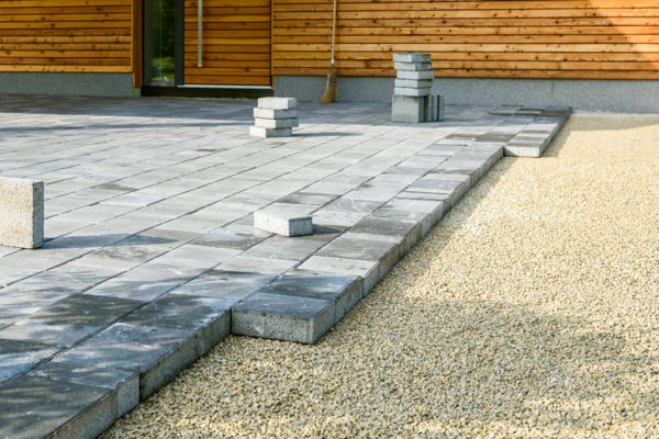Graue Pflastersteine werden auf einer Kiesschicht verlegt und bilden den Terrassenboden.