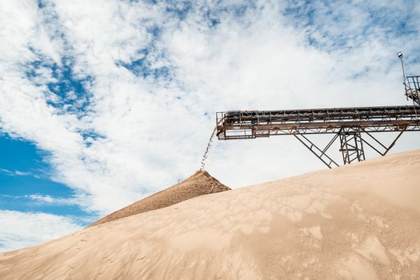 Im Hintergrund läuft ein Förderband das Quarzsand auf einen großen Sandhügel aufschüttet.