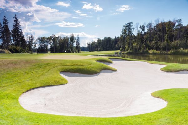 Ein Golfplatz umgeben von grüner Wiese und einem kleinen See.