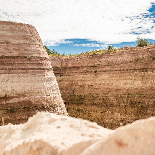 Steep, layered sandstone walls of a sand pit under a blue sky with light clouds.