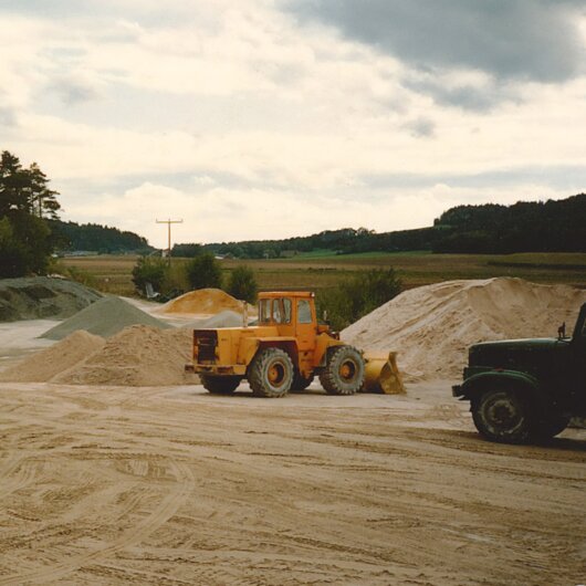 Construction site in a rural area with a yellow wheel loader and piles of sand and gravel.