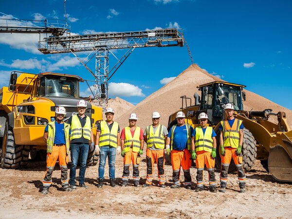 Team wearing hard hats and safety vests standing in front of heavy machinery at a sand quarry