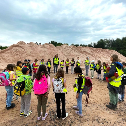 Group of schoolchildren wearing safety vests on a sandy site with sand piles in the background