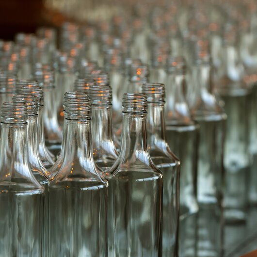 Rows of empty, clear glass bottles standing closely together in a production facility.