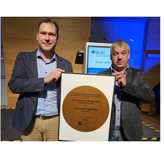 Two men hold a large certificate recognizing outstanding occupational safety achievements of the Wellmersdorf quartz sand plant.