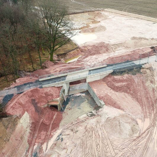 Aerial view of a sand quarry with a newly built concrete bridge, surrounded by forest and agricultural fields.