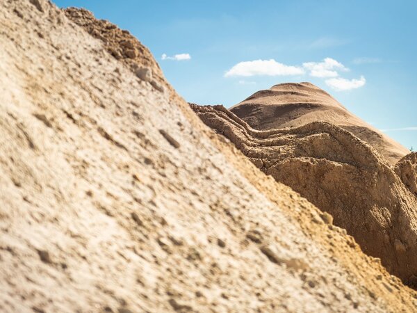 Close-up of large sand dunes under bright sunlight with a blue sky in the background.